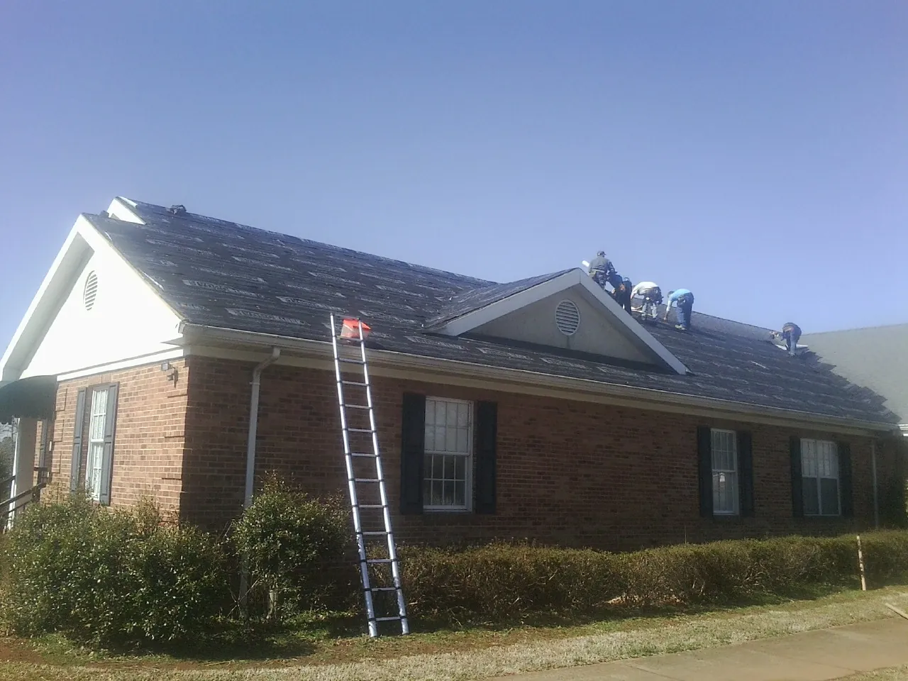 Crew tearing shingles off a brick ranch roof with a ladder set — Emergency Roof Repair work by our crew in New Hope