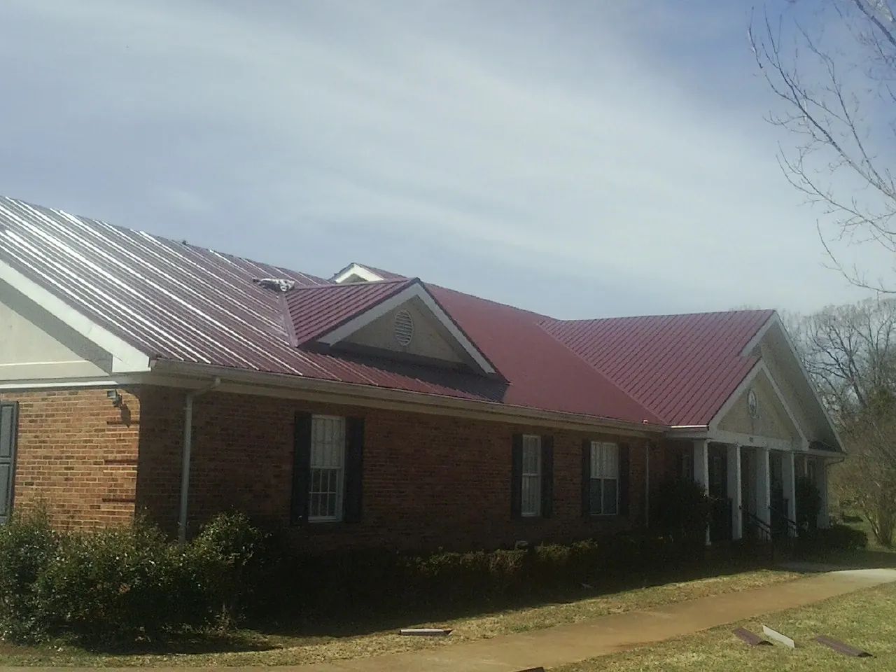 Red metal roof with gabled entries on a long brick building, from a Hail Damage Roof Repair job in New Hope