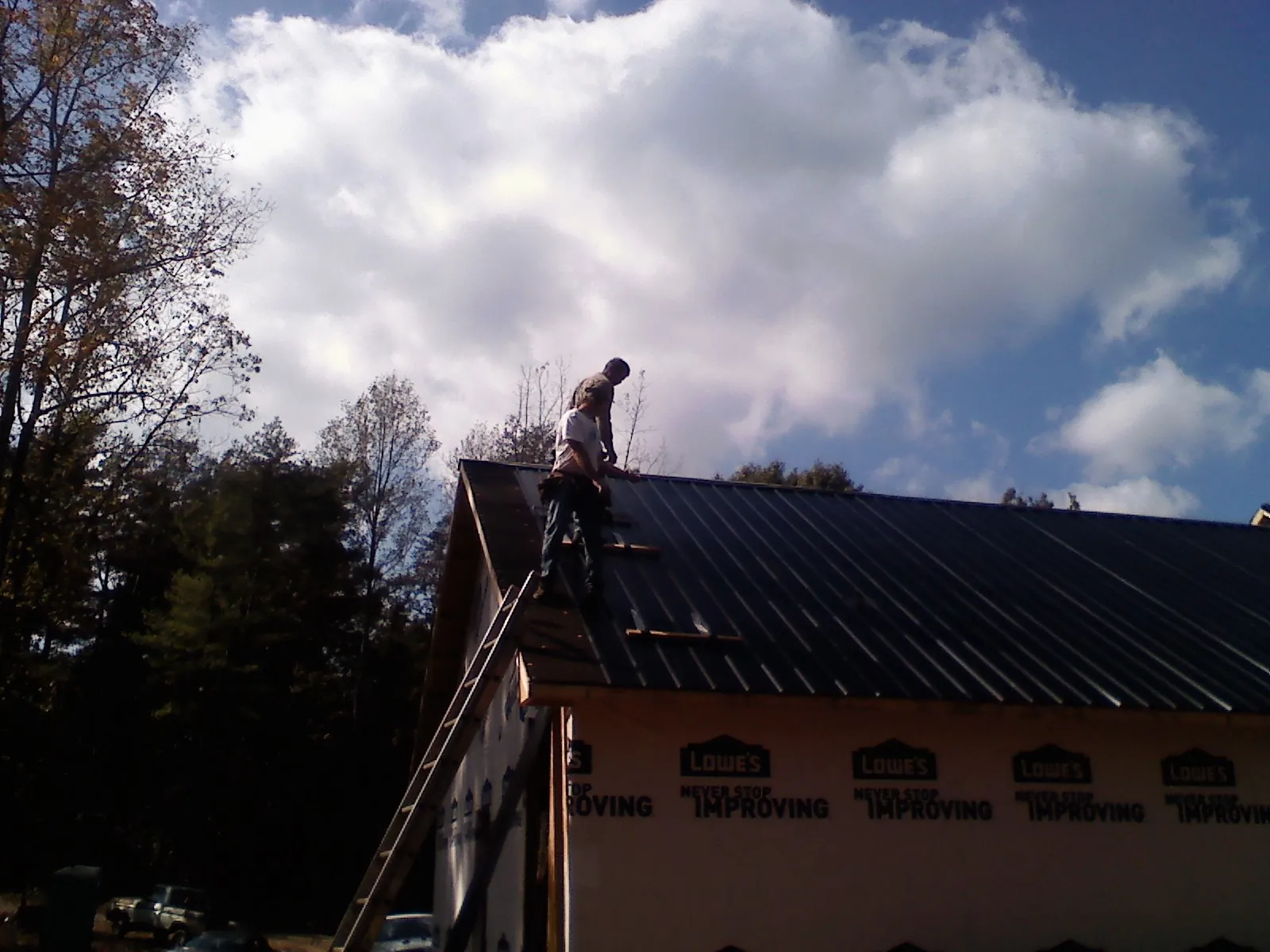Roofer fastening dark metal panels high against a cloudy sky, from a Roof Inspection job in New Hope