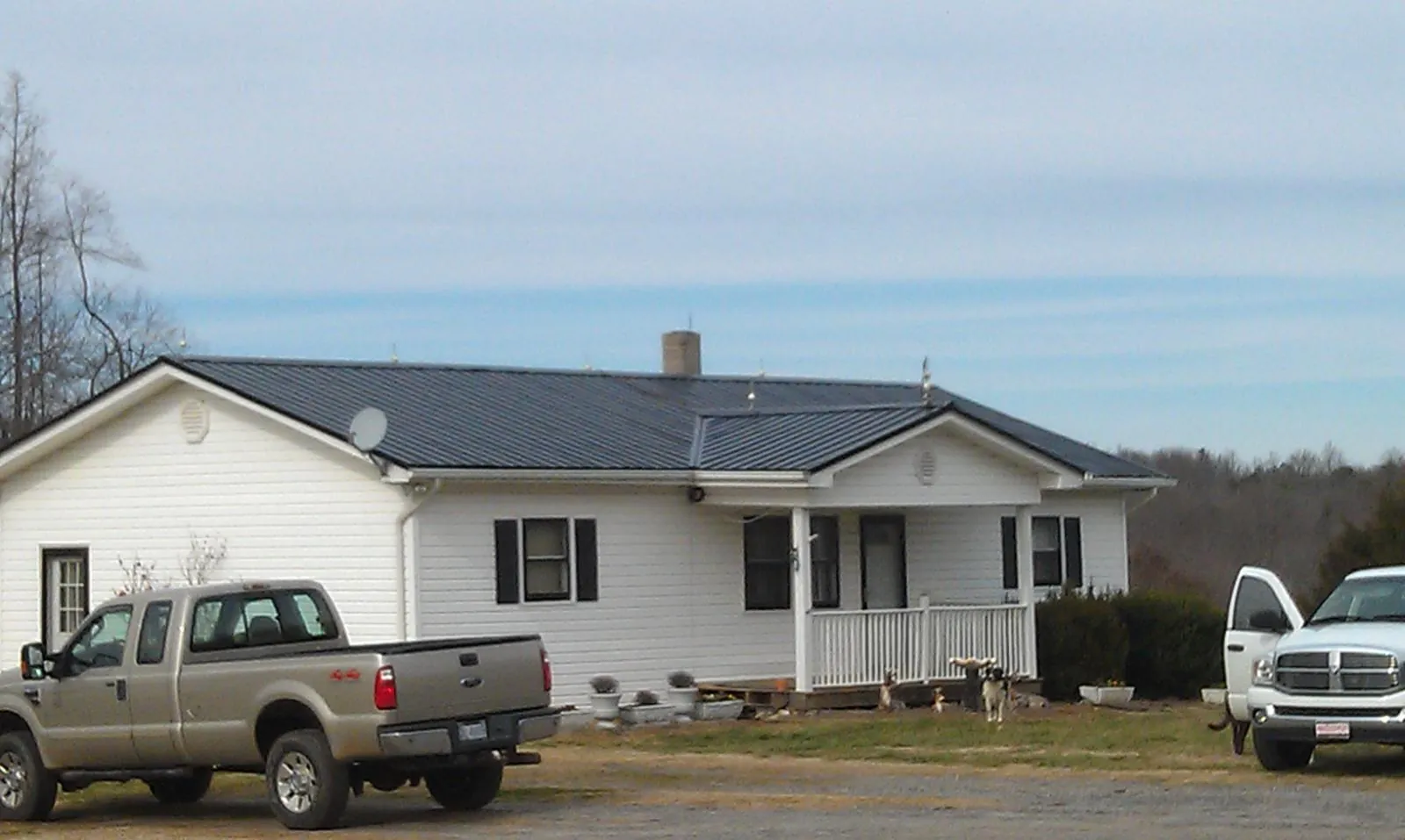 Finished dark metal roof on a white ranch home with work trucks parked in New Hope