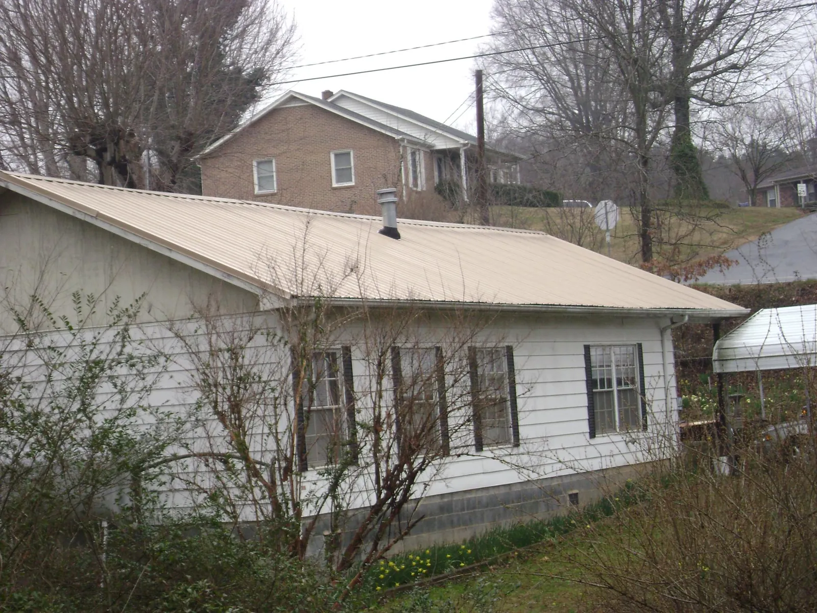Tan metal roof on a white sided house set into a hillside — Commercial Roofing by Roofing Brothers in New Hope